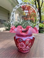 Front view of cranberry opalescent basket with twisted handle and ruffled rim, showing floral design.