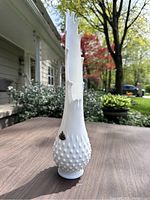 Front and side view of tall white milk glass Fenton vase with hobnail texture and swung top rim, displayed outdoors on a table.
