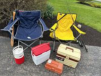 Wide view showing two camping chairs, coolers, tackle boxes, and wooden paddle.