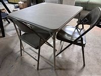 View of folding table with 2 metal folding chairs in a concrete floor room, showing overall condition and color.