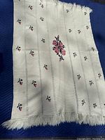 Full view of cream colored hand knitted afghan with rose motifs and fringe edges laid flat on a blue surface.