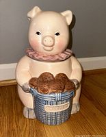 Front view of the pig ceramic cookie jar showing facial details, pink collar, and blue basket holding cookies.