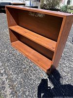 Front angle showing pine wood bookcase with visible sticker residue on back panel and fixed shelf.