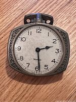 Front view showing silver dial with Arabic numerals and decorative leaf motifs on metal case.
