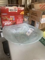 Angled side view of square white art glass bowl showing swirling white and translucent pattern and curved edges with measuring tape and surrounding boxes in background.