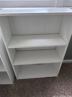 White bookshelf with three shelves. The middle shelf is adjustable with multiple drilled holes on the sides.
