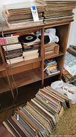 Wide view of wooden shelves packed with vinyl records and albums, some placed in boxes and plastic bags, additional stacks on the floor.