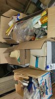 Cardboard boxes filled with art supplies, packaging, and miscellaneous items.