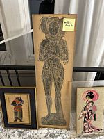 Photo showing three Asian art pieces: one long etching with a knight figure, and two framed textile artworks of Asian subjects.