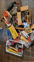 View of multiple cardboard boxes and plastic bags filled with various hand tools including hammers, punches, clamps, staple guns, and utility knives, all untested.