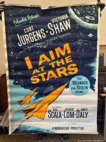 Front of 'I Aim at the Stars' movie poster showing title, actors, and rocket illustration on blue background.