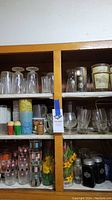 Front view of wooden cabinet shelves showing various mid-century modern glassware including patterned glasses and small condiments containers.