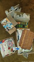 Overview shot showing six boxes filled with sewing patterns, notions, thread spools, and a wicker basket on a floor.
