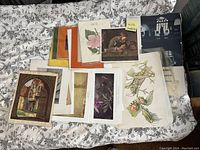 Wide overview of an assortment of small art posters spread on a bed, showing various styles including architectural and botanical.