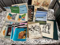 Image showing a collection of assorted prints spread on fabric, including colorful posters with automotive policy themes and small detailed black and white and color prints.