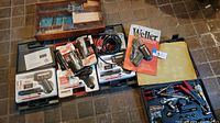 Photo showing multiple Weller soldering guns in plastic cases, solder tips, cords, and a wooden organizer with various metal tools inside.