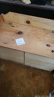 Photo of rectangular unpainted wooden storage chest with visible wood grain and knots, closed hinged lid, and side supports.