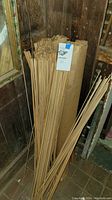 Bundle of wooden dowels standing upright next to wall with paper wrapping visible