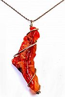 Close-up photo of raw orange agate pendant with wire wrap on metal chain.