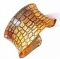 Close-up angle of gold-tone open cuff bracelet showing detailed cobra snake scale textured pattern with black etched lines on surface.