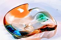 Top view of a freeform clear glass ashtray with orange, blue, and green color accents inside the glass.