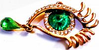 Close-up image of vintage eye-shaped brooch pendant showing green round rhinestone center, clear rhinestone border, gold-tone metal structure, and dangling teardrop-shaped green gem.