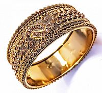 Close-up photo of the vintage Asian hinged bangle showing intricate raised filigree and ornamental patterns with textured background.