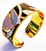 Close-up side angle of the vintage gold tone cuff bracelet revealing multi-colored enamel floral patterns on a black background.