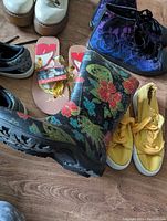 Assorted footwear including Sloggers floral rain boots, yellow sneakers, purple women's boots, Nike youth sneakers, and flip flops.
