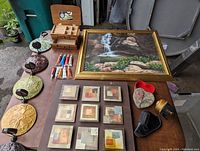 View of all items on table including framed picture, candle sconces, jewelry box, small framed mosaic art, heart box, holster, fishing reel, and repair tubes.