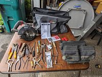 Overview of entire lot showing Porter Cable circular saw, carrying bag, toolbelt, hand tools, and manuals laid out on table