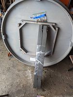 Bottom view of the round wood table top and underlying support frame with pack of screws.