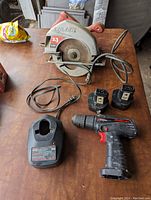 Photo showing Skilsaw circular saw, Snap-On cordless drill, two batteries, and charger on wooden surface.