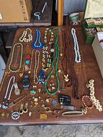 Full layout of vintage costume jewelry on brown table showing necklaces, bracelets, watches, rings, brooches, and earrings.