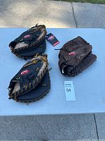 Three Rawlings baseball gloves displayed on a table, two black and tan and one brown.