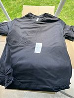 Black t-shirt laid on cardboard showing front view and paper tag