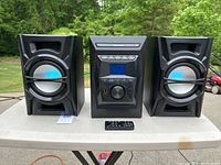 Front view of the Bluetooth stereo system showing central control unit flanked by two speakers on a table, with visible remote control in front.