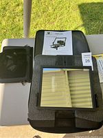 Overview of Glide Gear TMP 100 teleprompter kit with phone holder, glass mirror, instruction manual, and case on a white table outside.