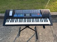 Front view of Casio CTK-511 keyboard on an X-style stand outdoors showing the control panel, keys, and built-in speakers.