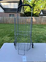 Front view of the metal collapsible cart standing upright showing wire grid sides, black padded handle, and two wheels.