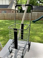 Front view of the Cruiser Cart collapsible metal wire shopping cart with black handle and wheels on outdoor table.