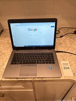 Front-facing open laptop on counter showing keyboard, touchpad, and display with Google homepage loaded