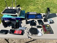 Photo of multiple electronic devices on a table including routers, network switch, power adapters, cables, Roku device, and RAM module.