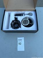 Open box displaying microphone, shock mount, and headphones inside foam padding.