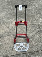 Red and silver Milwaukee folding hand truck standing with extended handle and metal base plate visible.