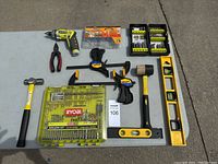 Full lot of various tools laid out on concrete including Ryobi drill, clamps, hammer, pliers, mallet, levels, drill bit kits, and screw/anchor kit.