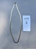 Full view of flat herringbone chain necklace laid out next to lot label