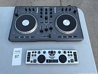 Photo of two Numark DJ controllers on a table: a larger black Mixtrack controller with two jog wheels and a smaller white DJ2GO controller with smaller jog wheels.