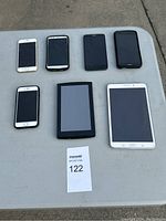 Seven devices displayed on table including five smartphones and two tablets for sale as parts with unknown functioning or registration status.
