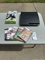 Photo showing the PlayStation 3 console, Xbox 360 games stacked, and new Xbox 360 controller with headset still in packaging.